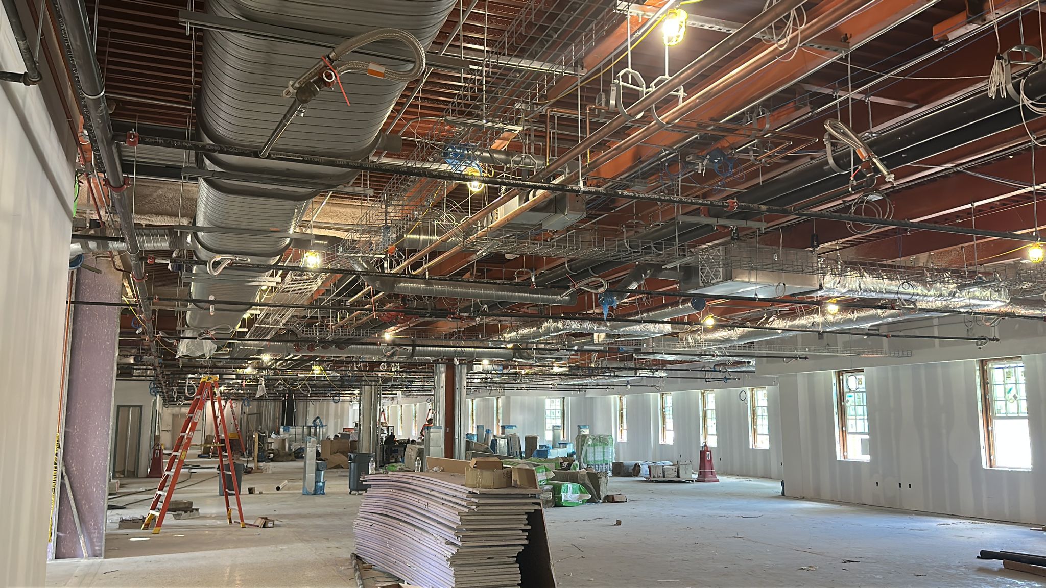 Commercial construction interior showing exposed ductwork, piping, cable trays, and active mechanical rough-in work